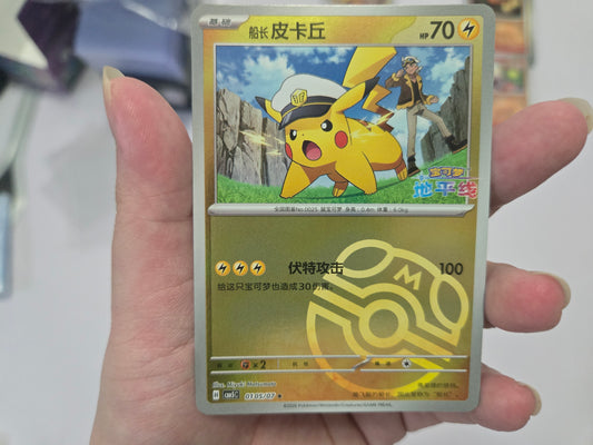 Pokémon trading card featuring Pikachu in Chinese text, with a blurred background showing a light-colored surface and some objects.