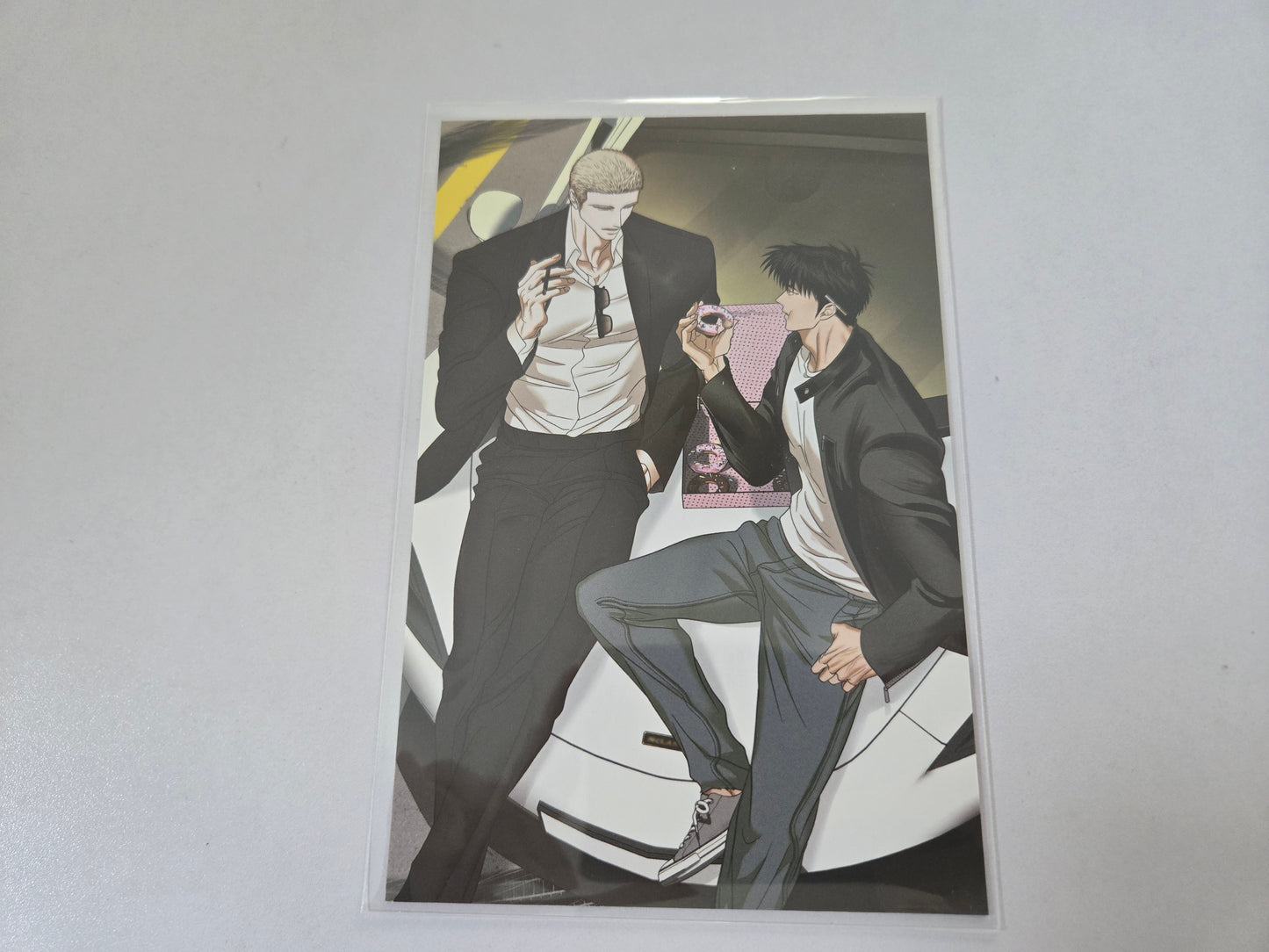 Jake and Shin gun in black leather jacket sitting close together on a white car.