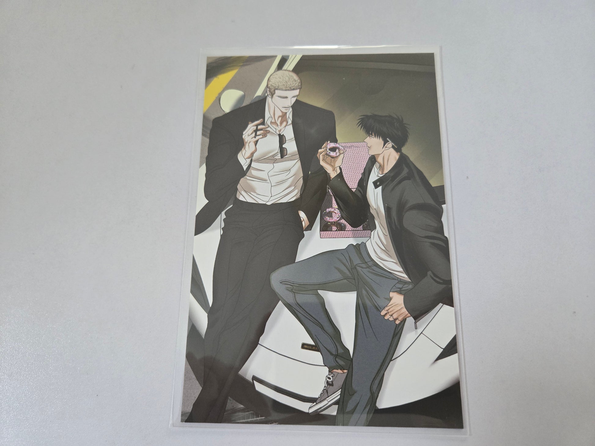 Jake and Shin gun in black leather jacket sitting close together on a white car.