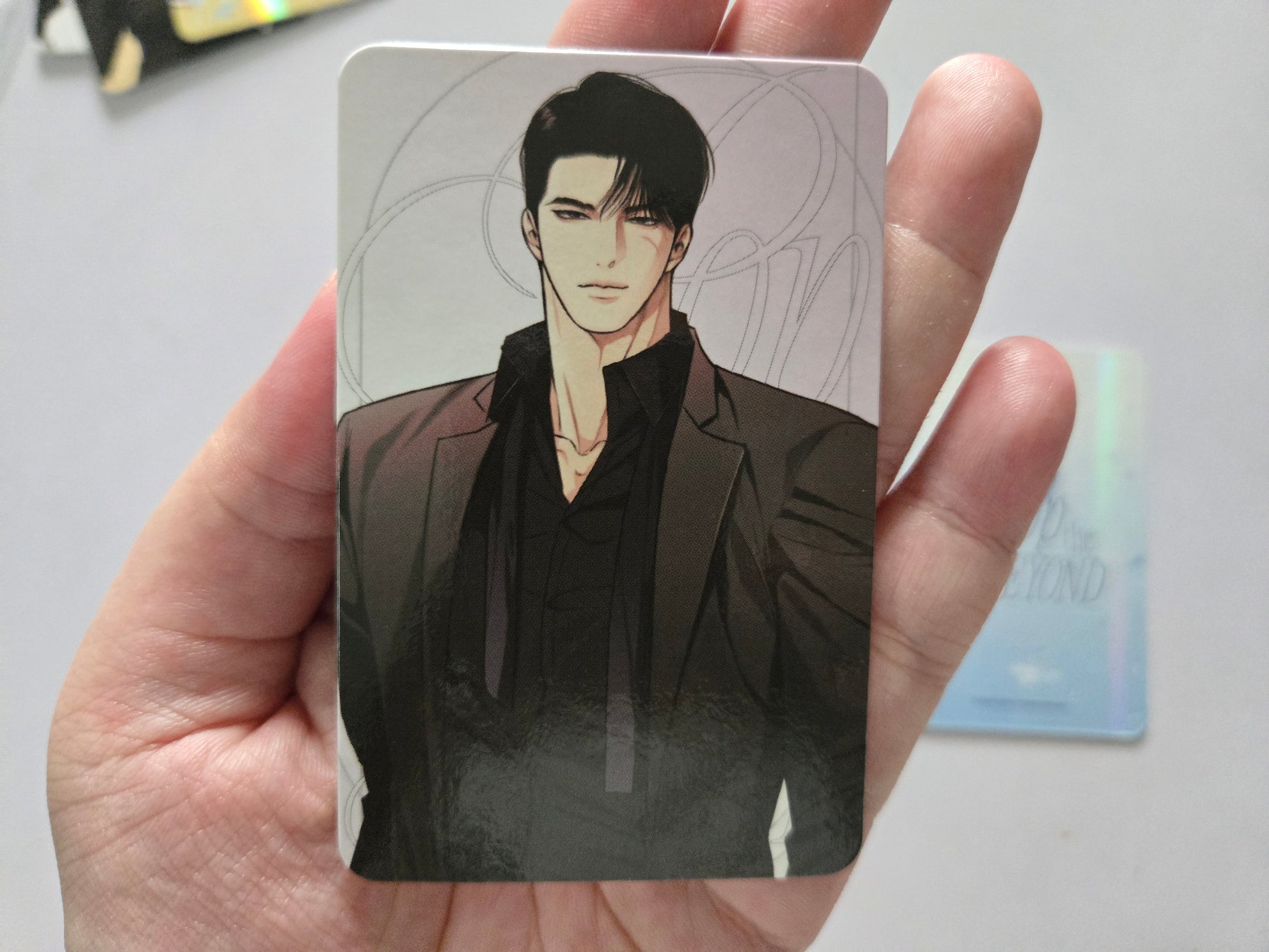 Tae seo in a dark suit. The card has rounded corners and is photographed against a light gray background with another blurred card visible in the distance.